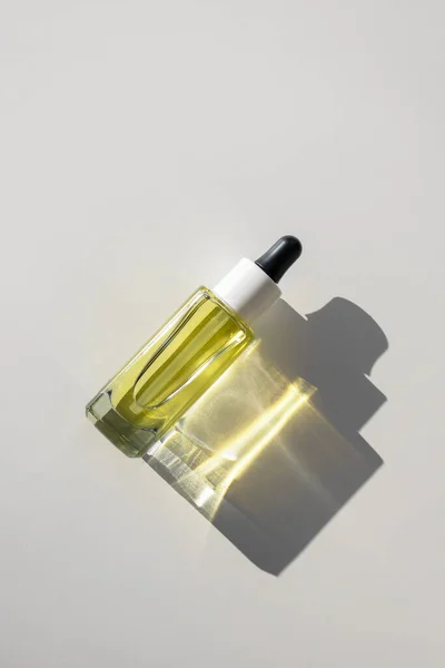 Botella de vidrio de suero de aceite amarillo facial con pipeta sobre fondo blanco con reflejo de rayo de sol brillante, vista superior — Foto de Stock