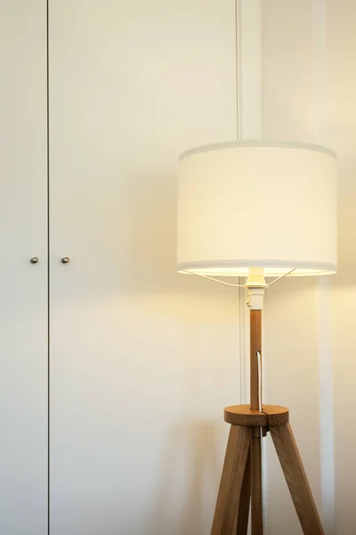 White floor lamp with wooden legs lights up. Minimalist interior details in domestic room