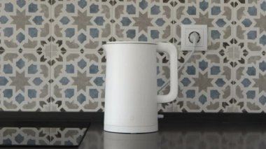 Modern mutfakta kadın eli beyaz elektrikli su ısıtıcısını çalıştırıyor.