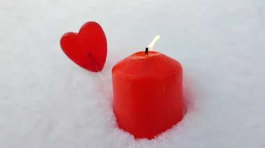 Karda kırmızı mum. Yanan mum. Kalp şekilli lolipop arka planda odak dışı.
