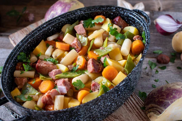 Homemade stew with root vegetable and meat. Delicious autumnal and wintry stew with root vegetable such as carrots, onion, sugar naps, black salsify, turnip and potatoes. cooked with smoked pork meat and served in a rustic stew pot on wooden table.