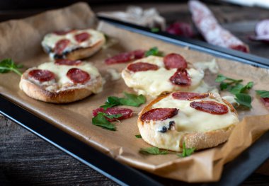 Peynirli ve salamlı ızgara ekmek. Fırında pişmiş İngiliz keki, organik İrlanda çedar peyniri ve İspanyol serrano salamı. Kırsal ahşap masadaki pişirme tepsisinde servis edilen, arka planı bulanık olan yakın plan görüntüsü