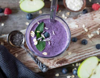 Sütlü proteinli sağlıklı kahvaltı içeceği. Sütlü protein, yulaf ezmesi, chia tohumu ve meyveli fitness kahvaltısı smoothie. Tahta masada kaşıkla içki bardağında servis edilmiş. Genel Görünüm
