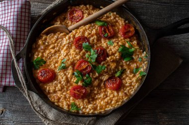 Tavada domatesli risotto. Parmesanlı rendelenmiş peynirli leziz domates pilavı ve üzerine kızarmış kiraz sosu. Ahşap bir masada yalıtılmış bir kırsal dökme demir tavada servis edilmiş. Genel Görünüm