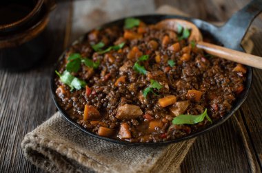 Tavuk göğsü ve sebzeli mercimek yahnisi. Sağlıklı ve yüksek protein zindelik gıdaları. İçinde mercimek, domates, soğan, sarımsak, bitki ve havuç olan lezzetli bir et yahnisi. Ahşap bir masanın üzerinde kırsal dökme demir bir tavada servis edilmiş..