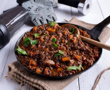 Glütensiz ve yüksek proteinli sıcak yemek ya da öğle yemeğinde mercimek, tavuk göğsü, sos ve sebzeli lezzetli bir güveç. Sallanan bir masanın üzerinde, dambıllar bir eldiven. 