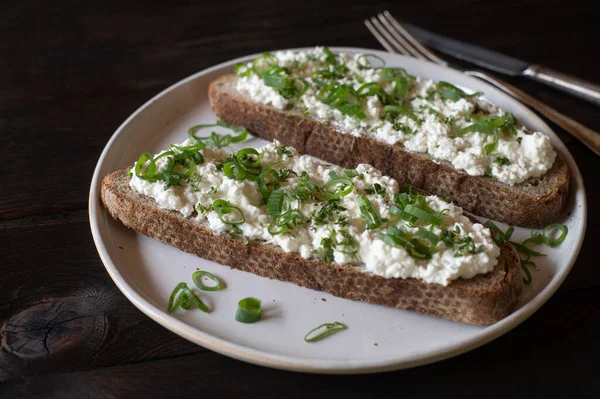Bread with cottages cheese and herbs. Delicious homemade and high protein fitness meal with german sourdough bread topped with low fat cottage cheese, chives and cress. Served on a plate isolated on wooden table.