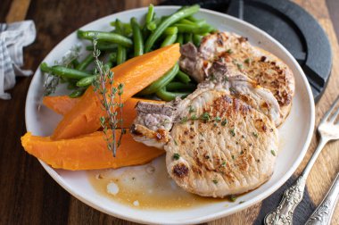 Akşam yemeği ya da öğle yemeği için spor yemeği. Spor beslenmesi için kas geliştirme yemeği, kızarmış domuz pirzolası, tatlı patates ve yeşil fasulye. Arka planda dambıl olan bir tabakta servis edilir..