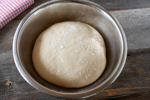 Rising yeast dough in a bowl after rest time served on wooden table background from above