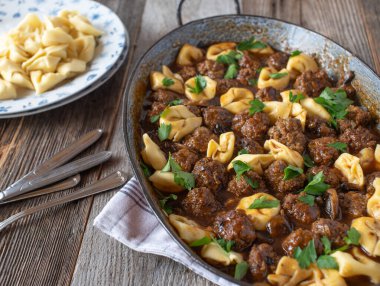 Makarna ve mantar soslu köfte, nefis ev yapımı leziz lezzetli yemek. Tahta masadaki güveçte servis edilmiş.. 