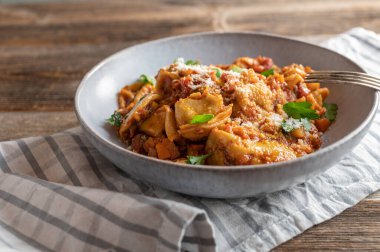 Tortellini tabağı. Lezzetli bir domates, sebze sosu. Parmesan peyniri ile kaplanmış ve ahşap masada çatallı bir tabakta servis edilmiş.. 