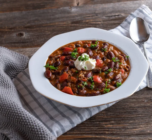 Bowl of chili con carne. Fresh cooked chili or spicy bean stew with ground beef, chili, bell pepers, onions, garlic and tomatoes. Served on a rustic plate or bowl on wooden table
