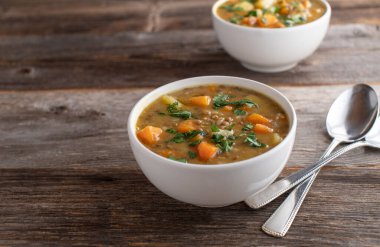 Taze ve ev yapımı vejetaryen ya da vejetaryen güveç, mercimek, sebze ve patates. Tahta masada izole edilmiş kaşıkla fotokopi alanı olan bir kasede servis ediliyor.