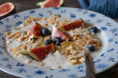 Ev yapımı taze yulaf lapası, incir, yaban mersini, badem. Masada kaşıkla servis ediliyor. Bulanık arkaplan ile yakın plan