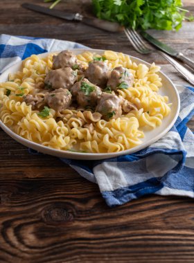 Delicious homemade cooked meatball dish with cream sauce and pasta. Swedish Kttbullar meal. Served on a plate isolated on wooden table
