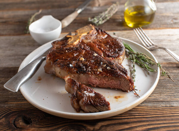 Traditional pan fried and dry aged porterhouse steak or t-bone steak served with salt and pepper seasoning on a plate on rustic and wooden table background