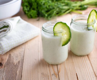 Low carb protein smoothie. Delicious refreshment drink with dieting or healthy lifestyle with a blended drink made with fresh cucumber, yogurt, garlic, herbs and lemon juice. Served in a glass jar on wooden table