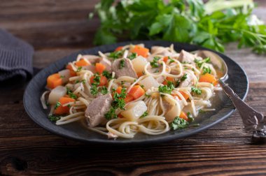 Koyu bir tabakta tavuk çorbası ve ahşap masada izole edilmiş kaşık.