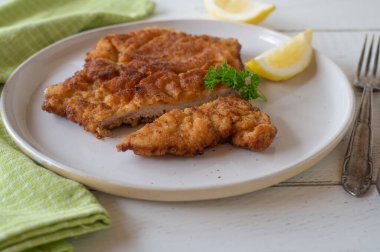 Viyana şnitzeli. Beyaz bir tabakta limon ve müzakere ile servis edilen ev yapımı ve taze tava. Beyaz masada tek başına servis edilmiş. Ön görünüm ve yakın plan