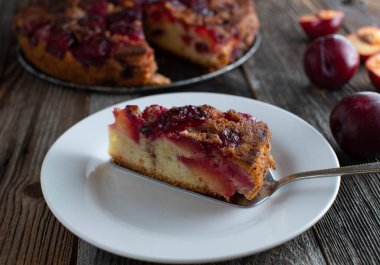 Tabakta bir parça meyveli kek. Taze ve ev yapımı erikli kek, baş aşağı. Ahşap masa arkasında kek sunucusu olan bir tabakta servis edilmiş. Yemek hazır..