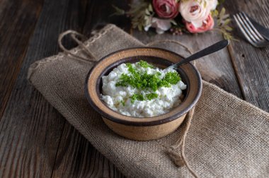Köy taşından yapılmış bir kasede kaşıkla servis edilen doğranmış otlarla servis edilen süzme peynir ahşap masa zemininde fotokopi alanı ile izole edilmiş. Yemek hazır.