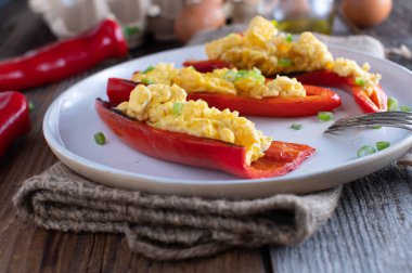 Sağlıklı ve ev yapımı düşük karbonhidratlı ya da çırpılmış yumurtayla doldurulmuş kızarmış kırmızı dolmalık biberli ketojenik kahvaltı. Tahta masada bir tabakta servis edilmiş. Yemek hazır.
