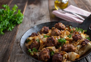 Tavada kızarmış köfte ve lahana ile taşralı ve lezzetli et yemeği. Koyu ahşap masa zemininde demir tavada servis edilmiş. Kopyalama alanı ile yakın görünüm