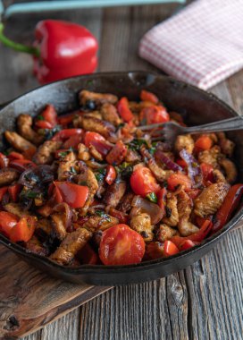 Düşük karbonhidrat diyeti için sağlıklı tava, kızarmış et ve kırmızı soğan, dolmalık biber, domates ve pırasa gibi akdeniz sebzeleri. Tahta masada, dökme demir tavada servis edilir..