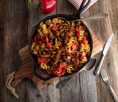 Dökme demir tavada sebzeli et ve makarna tavası. Lezzetli ve sağlıklı hindi göğsü, erişte ve sebzelerle pişirilmiş bir tencere yemek, ahşap masadaki dökme demir bir tavada servis edilir. Kopyalama alanı ile genel görünüm