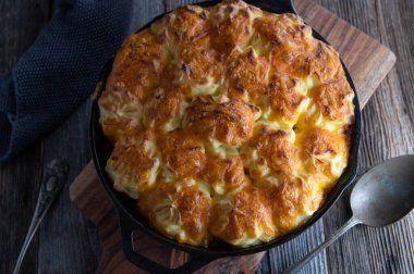Geleneksel İrlanda baharatlı çoban pastası patates çedar peyniri soslu. Koyu ahşap masa zemininde kırsal dökme demir bir tavada servis edilmiş. Yakın çekim ve genel görünüm
