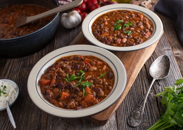 Bean stew with minced meat, vegetables and spicy tomato sauce. Served on plates on rustic and wooden table background