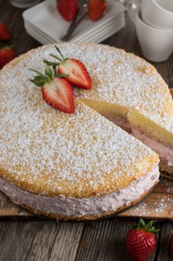 Çilekli kremalı pasta. Taze ve ev yapımı fırınlanmış ve kırsal ve ahşap masa arkasında servis edilmiş. Dikey resim