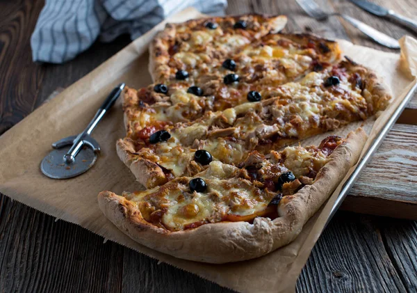 Homemade pizza with tuna, tomatoes, onions, black olives and mozzarella cheese. Served with pizza cutter on a baking tray on wooden table background.