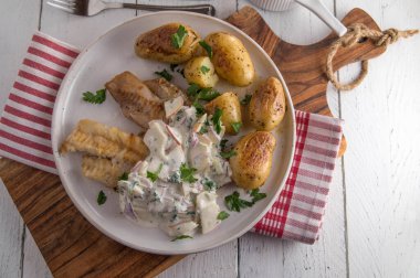 Ekşi krema, elma, soğan ve bitki soslu kızarmış kömür balığı. Kızarmış patatesle servis edilmiş, beyaz ahşap masa arkasında izole edilmiş bir tabakta.