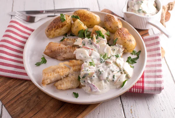 Ekşi kremalı, elmalı, soğanlı, sebze soslu ve patatesli kızarmış balık. Beyaz masa arkaplanındaki bir tabakta servis edildi