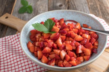 Sağlıklı meyve salatası ya da taze doğranmış ve marine edilmiş çilekli çilekli çilek. Kırsal ve ahşap masa zemininde fotokopi alanı ile izole edilmiş kaşıkla servis edilen bir kasede.