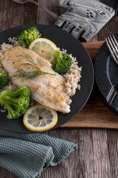 Body building meal with muscle building and fat loss with seared whitefish fillet, brown rice and broccoli. Served on a dark plate with dumbbell on wooden table. Top view with copy space