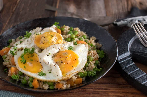Body building meal with fried eggs, brown rice and vegetables. Served in a rustic iron pan on wooden table background with dumbbell. Closeup view