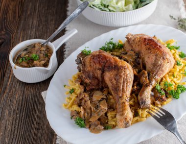 Kızarmış tavuk budu, kremalı soğan sosu ve makarna. Geleneksel ev yapımı kırsal ve ahşap masa arka planında pişirilip servis ediliyor. Üst görünüm