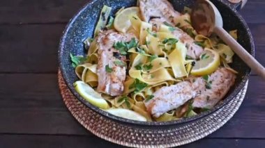 Balıklı makarna. Sarımsaklı zeytinyağlı sarımsaklı makarna soslu kırmızı balık filetosu. Tahta bir masada izole edilmiş bir tavada servis edilmiş. Gerçek zamanlı ve zoom yaparak uzaklaşmış.