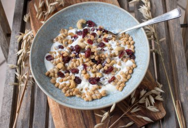 Kızılcık, kaju ve yoğurtlu puf yulaf ezmesi. Kırsal ve ahşap arka planda kaşıkla bir kasede servis edilmiş.