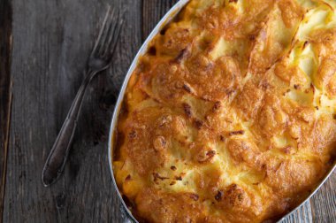 Potato casserole with ground beef, vegetables filling. Served in a rustic casserole dish isolated on wooden background. Table top view with copy space