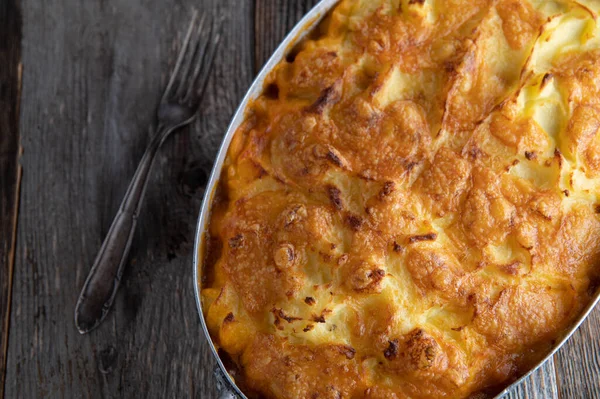Potato casserole with ground beef, vegetables filling. Served in a rustic casserole dish isolated on wooden background. Table top view with copy space