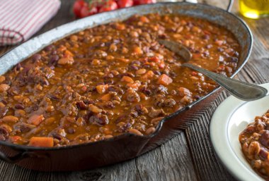 Delicious and spicy ground beef stew with kidney beans, carrots, tomatoes, bell peppers, onion and garlic. Served in a rustic and old fashioned cooking pan on wooden table