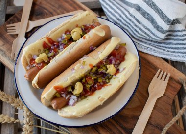 Hot dog with cheese, pickles, ketchup, mustard and ketchup. Homemade fresh cooked. Served on a rustic plate on wooden background