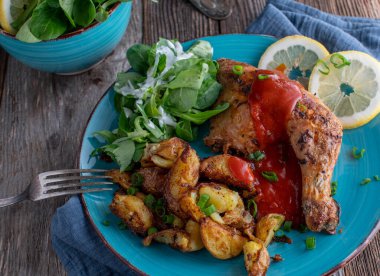 Roasted chicken leg with german curry sauce, fried potatoes and a green salad with sour cream dressing. Served on a plate isolated on wooden table. Top view