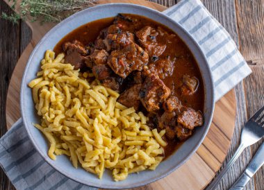 Hungarian goulash with german spaetzle noodles on a plate. Fresh and homemade cooked. Served isolated on wooden table