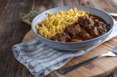 Homemade fresh cooked hungarian pork goulash with german spaetzle noodle. Served on a plate isolated on wooden table background with copy space