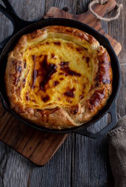 Puff pastry cake or tart with cheesecake filling baked in a cast iron pan and served isolated on dark wooden background