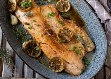 Roasted half salmon fillet with olive oil, herbs, garlic and lemon. Served in a rustic roasting pan on wooden background